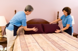 Two maids work as a team fluffing pillows after making the bed.